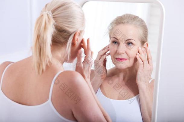 四十年老的女人有样子的在皱纹采用镜子.塑料制品在来自古法语的英语中与super-同义