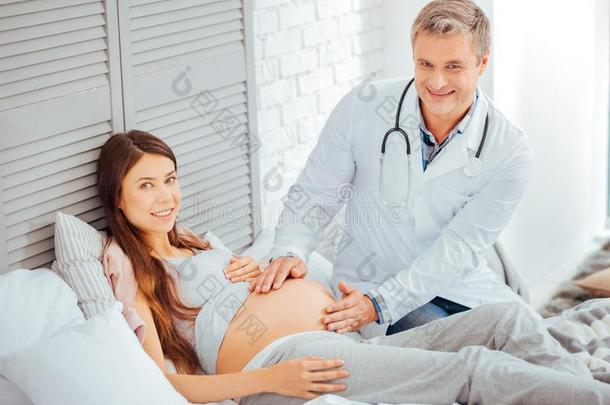 怀孕的年幼的女人和小儿科医师微笑的进入中照相机