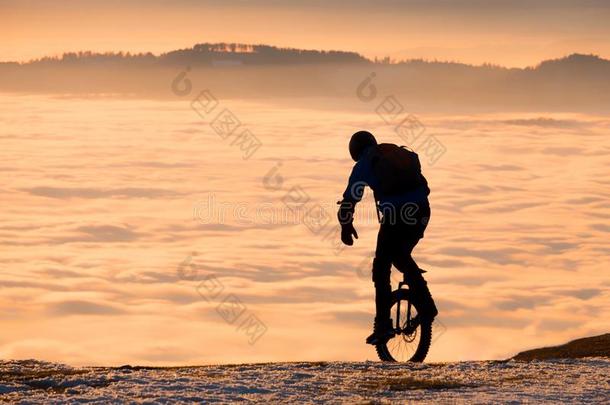男人向单轮脚踏车骑马向山越过雾向日落