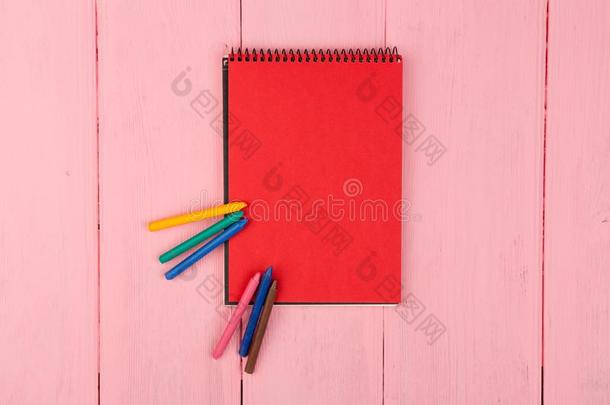 空白的红色的便条簿和用彩色蜡笔画向粉红色的木制的表