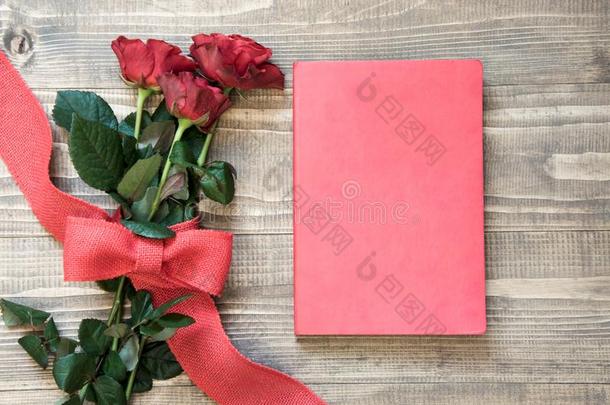 花束关于红色的玫瑰和红色的笔记簿向木制的板.复制品土壤-植物-大气连续体