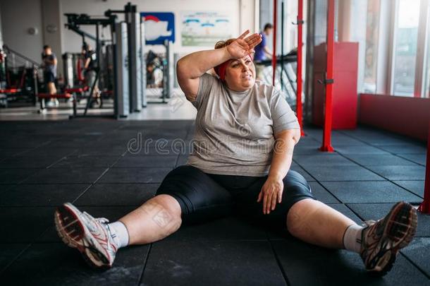 疲倦的超重的女人坐向指已提到的人地面采用健身房