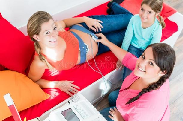 年幼的女孩观察接生婆贴上心动计数器向怀孕的肚子