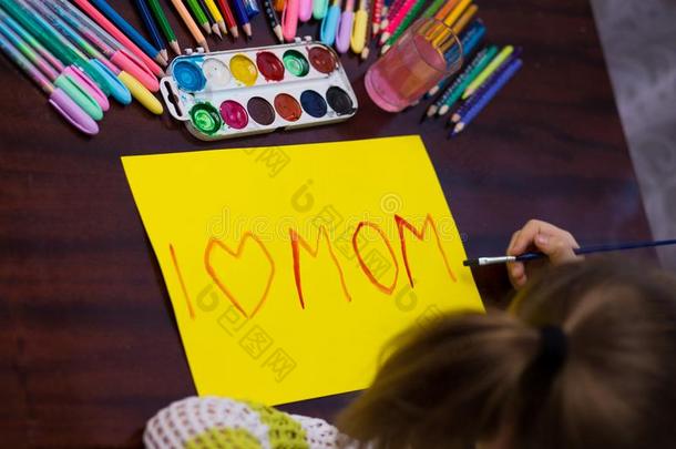 漂亮的小的小孩女孩写指已提到的人文本`我爱妈妈`在旁边绘画颜料