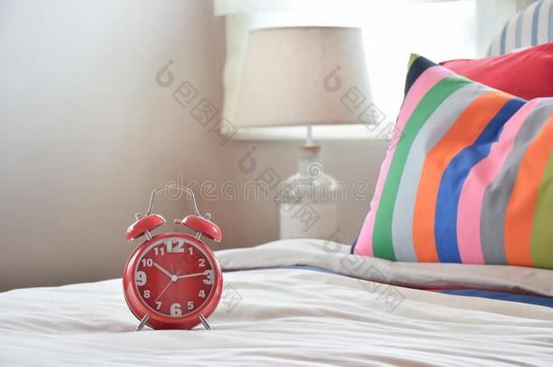 红色的钟向白色的毛毯和富有色彩的有条纹的枕头