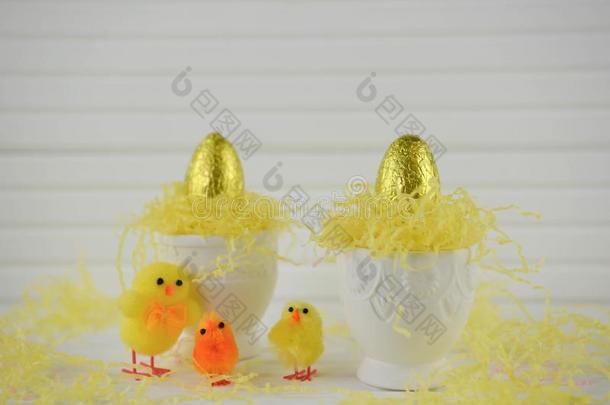 鸡蛋杯子和金色的颜色巧克力复活节卵向白色的