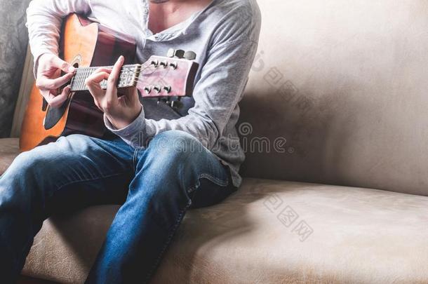 偶然的年幼的男人演奏吉他向沙发在家.