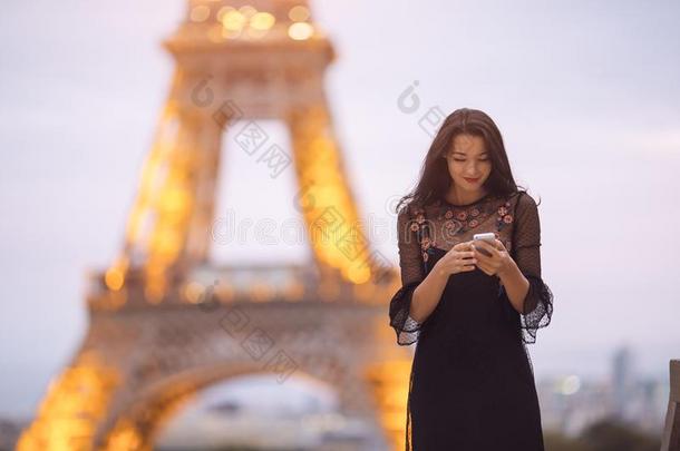 旅行女人使用智能手机在近处指已提到的人Eiffel语言塔和旋转木马