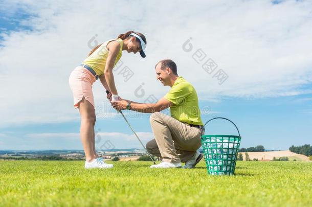 年幼的女人锻炼指已提到的人高尔夫球摇摆帮助在旁边她指导者