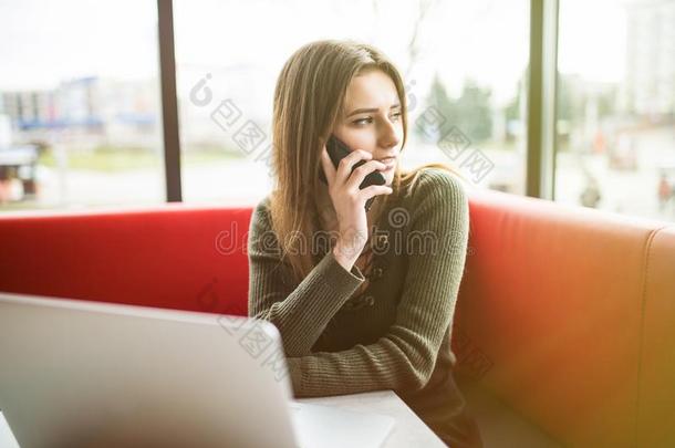 幸福的女人使用便携式电脑和电话采用咖啡馆.年幼的美丽的女孩