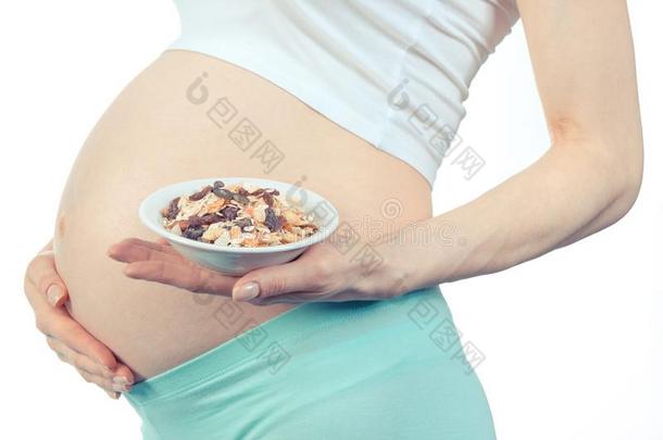 怀孕的女人和发嘎吱嘎吱声的牛奶什锦早餐采用玻璃碗,健康的坚果
