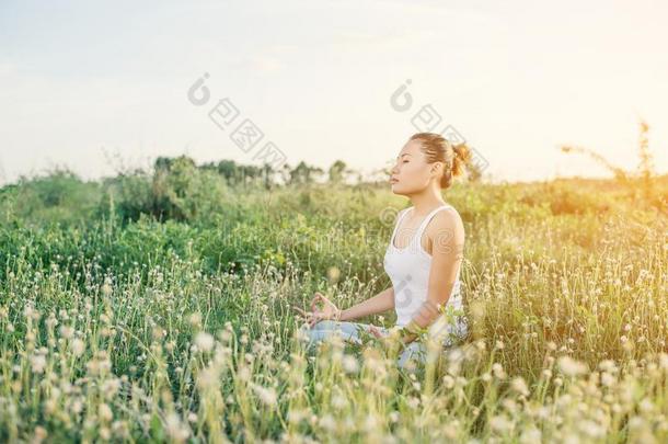 年幼的瑜伽女人开业的瑜伽向指已提到的人草地日落.