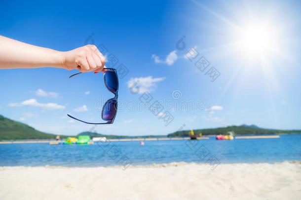 手拿住太阳镜和沙的海滩