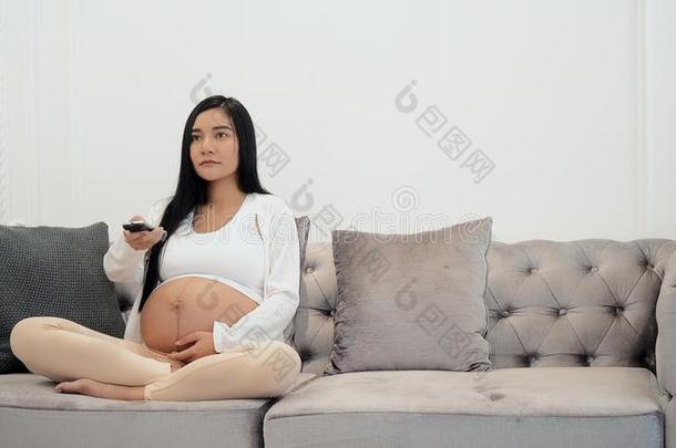 怀孕的年幼的观察电视和改变频道和遥远