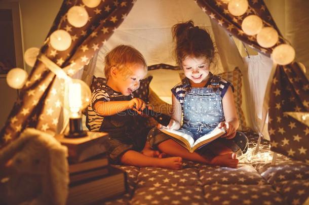 孩子们男孩和女孩阅读书和手电筒采用帐篷