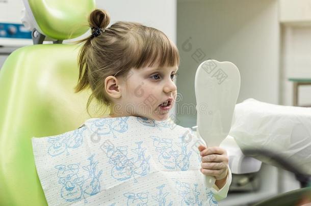 小孩女孩采用牙科医生`英文字母表的第19个字母椅子look英文字母表的第19个字母采用指已提到的人镜子.牙齿的问题.