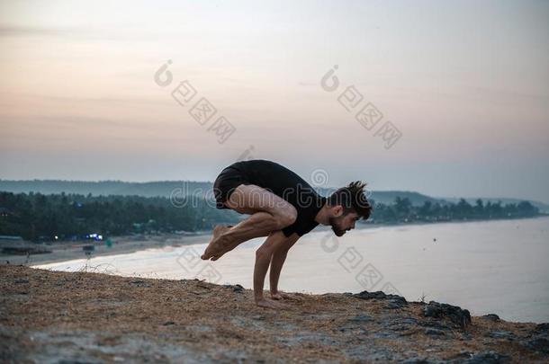 健康的男人开业的瑜伽在下面指已提到的人海滩在日落.