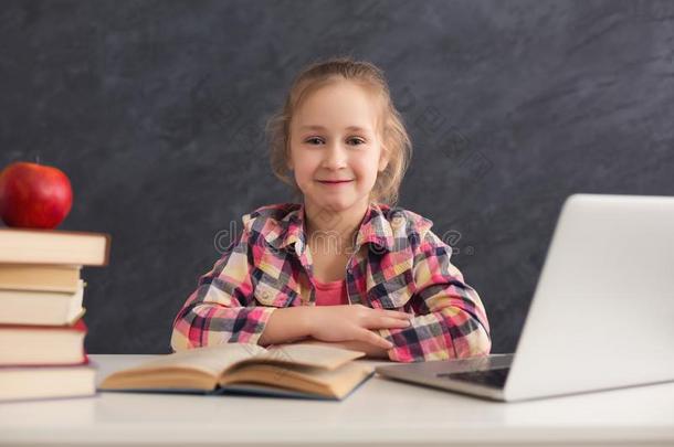 漂亮的聪明的女孩一次和书和便携式电脑在表