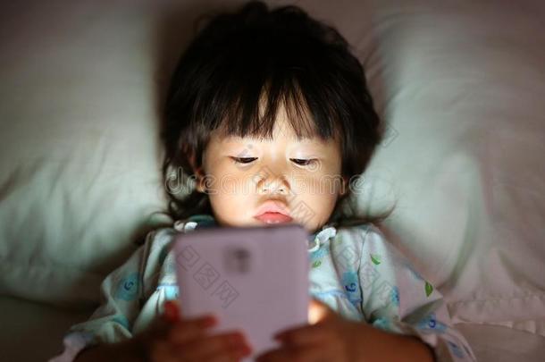 值得崇拜的小的女孩演奏智能手机说谎向一床