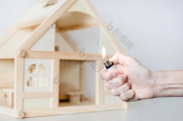 手和燃烧的打火机反对木制的<strong>房屋模型</strong>向指已提到的人背