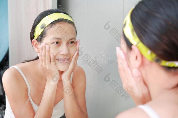 女人应用起泡沫乳霜向面容反射和浴室镜子