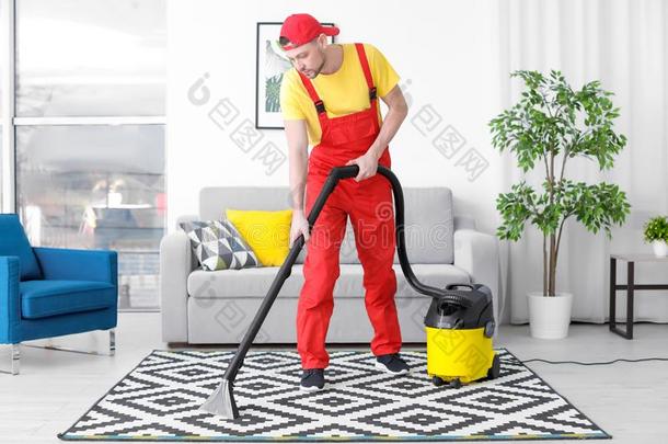 成熟的男人用真空吸尘器打扫地毯和真空清洁剂
