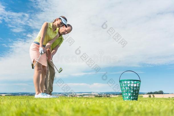 年幼的女人锻炼指已提到的人高尔夫球摇摆帮助在旁边她指导者