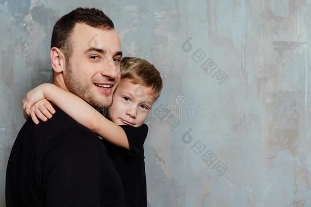 父亲和儿子拥抱儿子向灰色墙背景.Fashi向妈