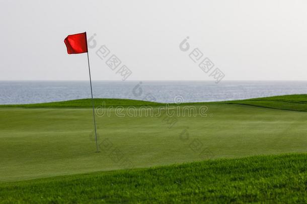 高尔夫球课程和绿色的草和红色的钉旗,海背景