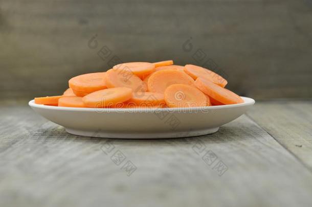 白色的盘子和将切开胡萝卜薄的向木制的背景