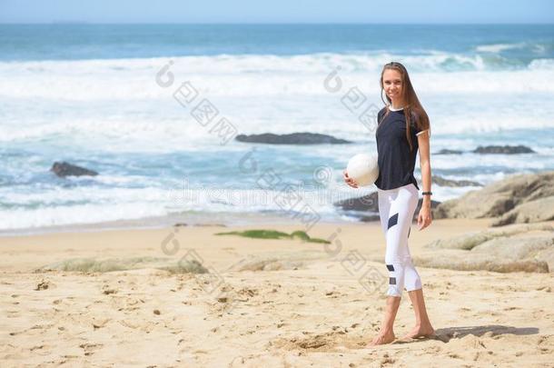 微笑的积极的年幼的女人向指已提到的人海滩和排球球