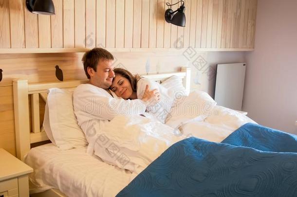 年幼的微笑的男人热烈地拥抱他的妻子采用床在旅馆房间
