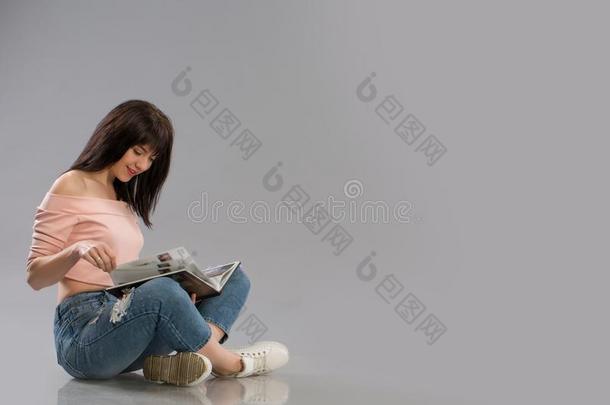 年幼的女人令人轻松的向地面阅<strong>读书</strong>向灰色的<strong>背景</strong>