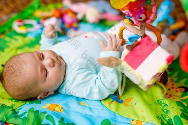 漂亮的值得崇拜的新生的婴儿演奏向富有色彩的玩具健身房
