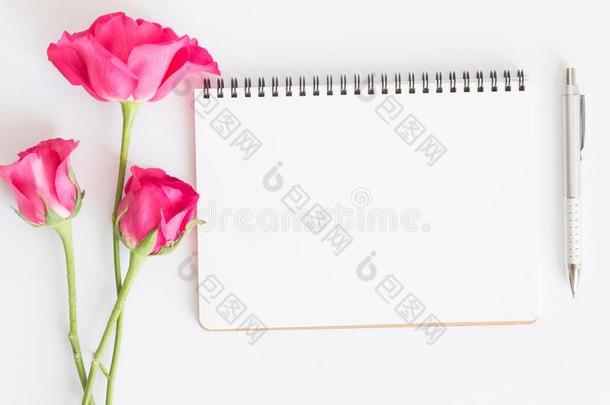空白的笔记簿和粉红色的玫瑰和笔向白色的背景,平的