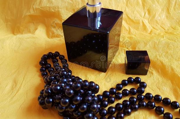 黑的珍珠necklale和香水瓶子向黄色的背景