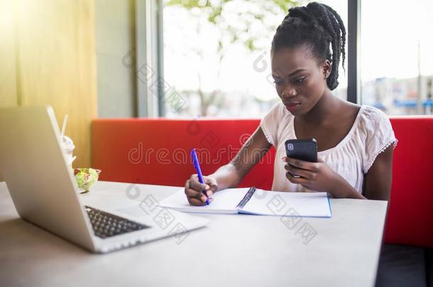 年幼的美丽的非洲式发型-美国人女人使用便携式电脑和文字采用