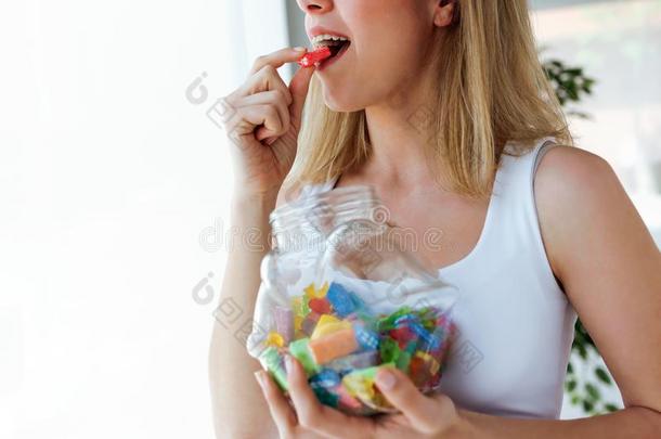 漂亮的年幼的女人吃富有色彩的果冻结晶糖在家.有瘾的人