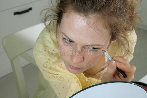 年幼的美丽的女人做化妆采用前面关于一镜子一t家.