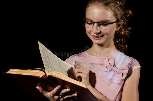 可爱的小的女孩起立和读书越过黑暗的背景