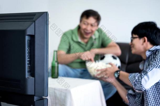 年幼的亚洲人男人和父亲观察<strong>足球比赛</strong>向television电视机和欢呼