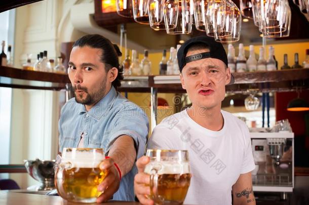 两个酒吧间销售酒精饮料的人制造有趣的幽默的面容和提议啤酒.