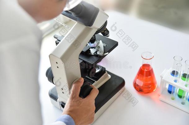 年幼的男人科学家有样子的通过一显微镜.
