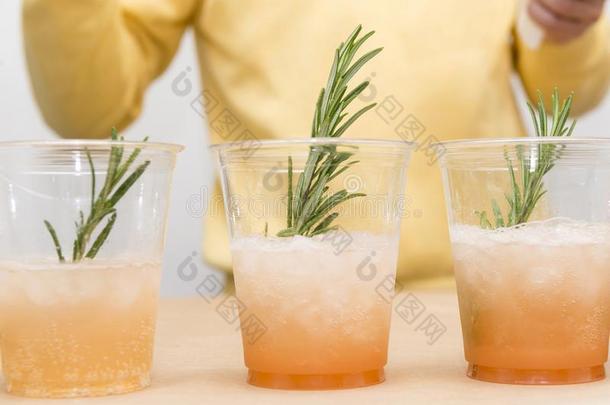 3杯子塑料制品和黄色的鸡尾酒和冰和一小树枝关于玫瑰
