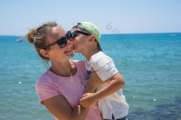 微笑的年幼的母亲吻婴儿在近处指已提到的人海.幸福的夏天