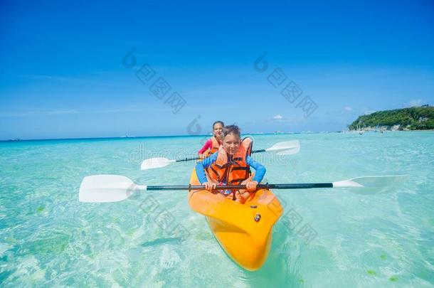 幸福的<strong>男孩</strong>和女孩皮艇运动在热带的海向黄色的爱斯基摩单人划子