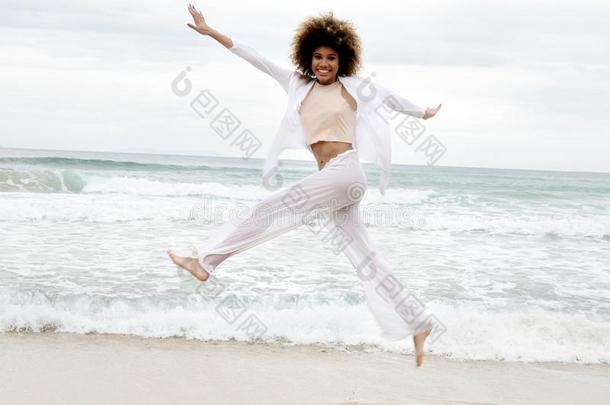 美丽的女孩和非洲式发型头发和白色的衣服跳向指已提到的人海滩