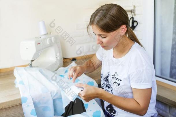 年幼的女人缝纫衣服和缝纫机器.