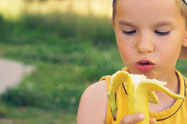 小的男孩吃香蕉,有样子的在照相机和幸福的面容,对有把握