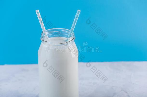 玻璃瓶子关于新鲜的奶和两个稻草向蓝色背景.英语字母表的第3个字母